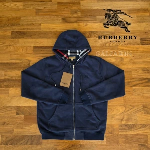 Marinblå Burberry Hoodie  - Letar du efter en stilren och lyxig hoodie? Denna helt nya marinblåa Burberry-hoodie kombinerar elegans med hög komfort. Den har Burberrys ikoniska rutmönster i fodret och en diskret logga på bröstet för en exklusiv touch. Liten i storleken! Tillverkad av mjukt, slitstarkt material och utrustad med dragkedja samt huva – både praktisk och stilfull.  📌 Skick: Ny med taggar. 📦 Snabb leverans – skickas samma dag!