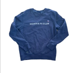 Blå sweatshirt från Morris R. Club - Snygg blå sweatshirt från Morris R. Club med tryckt logga och emblem på bröstet. Tröjan har rund halsringning, ribbade muddar och är tillverkad i mjuk bomull. Perfekt för en avslappnad och stilren look.