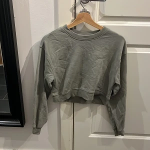 Grön croppad sweatshirt från H&M Divided - Snygg grön croppad sweatshirt från H&M Divided med broderad text 'original' på bröstet. Tröjan har ribbade muddar vid hals, ärmslut och nederkant samt långärmad passform. Perfekt för en chill och avslappnad stil. Har andvänds lite.😁