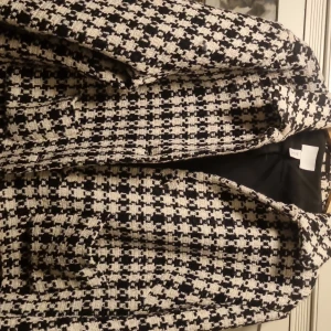 Rutig kavajjacka från H&M, storlek L - Snygg rutig kavajjacka från H&M i svart och beige. Jackan har klassisk krage, långärmad design och är fodrad med svart tyg på insidan. Materialet är grovt vävt och ger en cool, trendig look. Perfekt för dig som gillar statement-plagg och vill sticka ut.