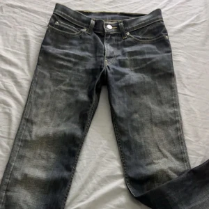 Levi's 501 svarta jeans med slitningar - Säljer ett par Levi's 501 jeans i svart tvättad denim med snygga slitningar. Jeansen har raka ben, fem fickor och den ikoniska läderpatchen bak i midjan. Perfekt för dig som gillar en tidlös och avslappnad look.