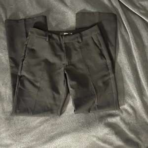 Svarta kostymbyxor från BikBok - Klassiska svarta kostymbyxor från BikBok i modellen Vera. Byxorna har raka ben, hällor för bälte och pressveck framtill. Perfekta för en clean och stilren look. Materialet är mjukt och följsamt, vilket gör dem bekväma hela dagen. Säljer då dom är för korta.