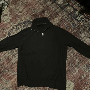Svart half zip polotröja Jack & Jones XL - Svart polotröja från Jack & Jones i storlek XL. Sitter bättre i storlek L till M. Tröjan har en snygg half zip-dragkedja framtill och är långärmad med ribbade muddar. Materialet är mjukt och känns som bomull eller syntet, perfekt för kyliga dagar. Enkel och stilren design som funkar till många outfits.