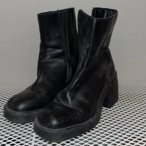 Svarta boots med klack och dragkedja - Svarta boots i skinn med chunky klack och rund tå. Snyggt minimalistisk design med dragkedja på sidan för enkel på- och avtagning. Perfekt för dig som gillar en edgy och stilren look. Passar till både jeans och kjol.