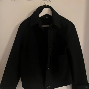 Svart midjacka  - Snygg svart midjacka  från lager 157 i storlek XS. Jackan har klassisk krage, stora fickor framtill och knäpps med knappar använd 2 gånger 