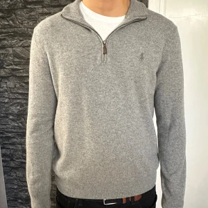 Grå halvziptröja Polo Ralph Lauren - Snygg grå stickad tröja från Polo Ralph Lauren med half zip och diskret logga på bröstet. Tröjan har lång ärm, ribbade muddar och hög krage. Perfekt för lager-på-lager. Köpt på Åhléns, ny pris 2500kr 