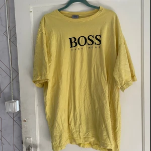 Gul t-shirt från Hugo Boss - Säljer en gul t-shirt från Hugo Boss i storlek XXL. T-shirten har en normal passform och är kortärmad. Den är gjord av bomull och har en stor BOSS-logga på framsidan. Perfekt för en avslappnad stil!