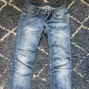 Blå jeans från Gang - Säljer ett par snygga blå jeans från Gang. De har en cool slitning på framsidan. Jeansen är i bra skick och har en normal passform. Innerbenslängd:68  Midjemått rakt över:36