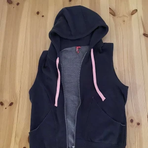 Mörkblå väst med huva från Energetics - Säljer en snygg mörkblå väst med huva från Energetics. Västen har en dragkedja framtill och rosa snören vid huvan. Den är i bra skick och väldigt bekväm att ha på sig.
