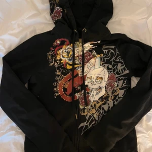 Svart hoodie Ed Hardy - Säljer en svart edhardy liknande hoodie. Den  har superfina guld detaljer och har inga defekter förutom att några diamanter har lossnat. Den är i storlek M men sitter som en xs/s. Säljer den här  hoodien för att den tyvärr är för liten på mig. Jag hade också kunna tänka mig att byta ut den här mot något liknande! Skriv vid frågor osv💞