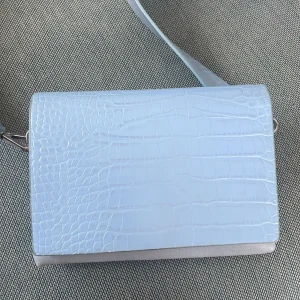 Ljusblå axelväska med krokodilmönster - Säljer en superfin ljusblå axelväska med krokodilmönster. Väskan har en bred axelrem och en magnetisk knappstängning. Insidan är ljusgrå och väskan är perfekt för både vardag och fest. Den är i bra och redo att användas direkt!