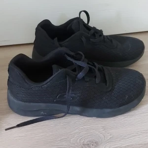Svarta sneakers från Skechers - Säljer ett par svarta sneakers från Skechers i storlek 38. Skorna är tillverkade av textil med en EVA-sula och har snörning framtill. De är i bra skick och perfekta för vardagsbruk eller träning.