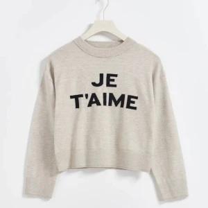 Beige tröja med texten 'JE T'AIME' - Säljer en superfin beige tröja med texten 'JE T'AIME' i svart på framsidan. Tröjan är croppad och har långa ärmar. Den är gjord av mjukt och skönt material, perfekt för höst och vinter. Passar både till jeans och kjol. Perfekt för en casual look eller en mysig dag hemma. Den är köpt på Gina Tricot för 229 och säljer för 150. 🧡