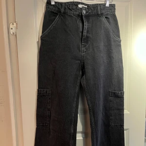Svarta cargopants från H&M - Säljer ett par svarta jeans från H&M i storlek EUR 38. Byxorna har en hög midja och är tillverkade i ett slitstarkt material. De har flera praktiska fickor och en avslappnad passform. Perfekta för en cool och bekväm stil!