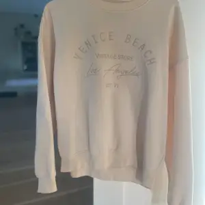 Säljer en snygg beige sweatshirt med tryck från Venice Beach Vintage Store. Den är supermjuk och bekväm, perfekt för en avslappnad look. Tröjan har långa ärmar och ribbade muddar vid ärmslut och nederkant. Passar perfekt till både jeans och leggings!