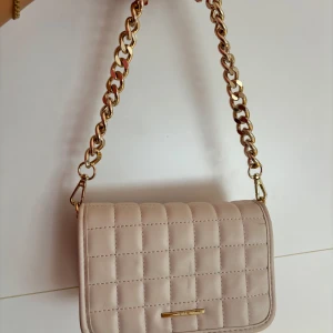 Axelremsväska  - Beige väska, inte använd så mycket så fint skick bara att den längre kedjan har tappat lite färg som syns på sista bilden. Den har två kedjor och den långa går inte att ta loss men funkar att ”gömma” den i väskan som jag gjort på sista bilden 💕