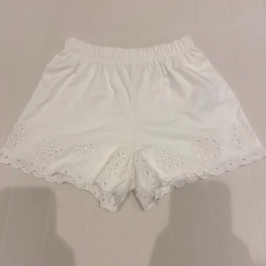 Vita shorts med spetsdetaljer - Säljer ett par superfina vita shorts med spetsdetaljer. De är högmidjade och har en elastisk midja för extra komfort. Perfekta för sommaren och kan lätt matchas med en söt topp eller blus. Shortsen är i nyskick och redo för en ny ägare!