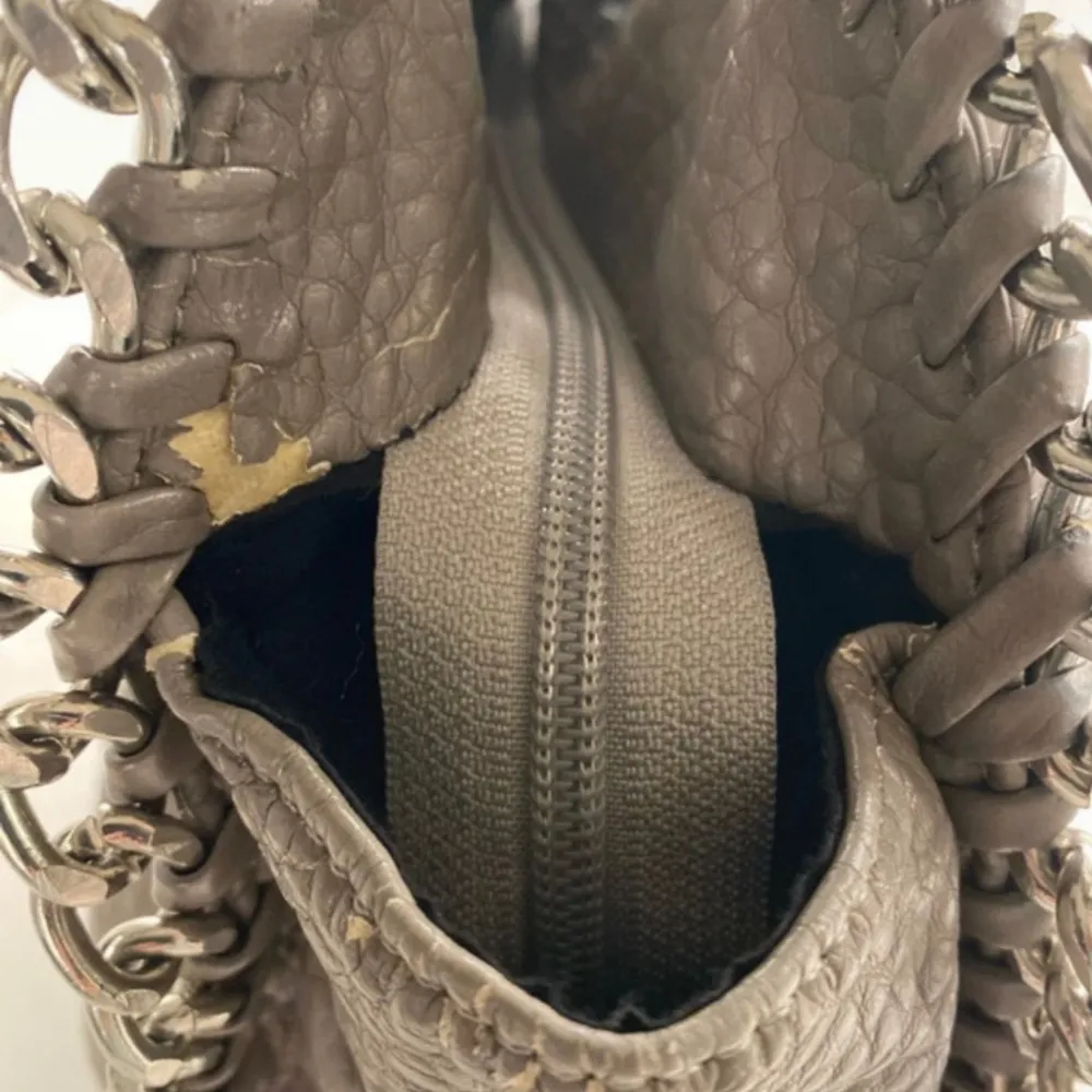 Snygg beige axelväska med coola kedjedetaljer längs kanterna. Väskan har en praktisk dragkedja på baksidan för extra förvaring. Perfekt för att ge din outfit en edgy touch. Se tre sista bilder för defekter. Nypris 599kr!. Laukut & Käsilaukut.