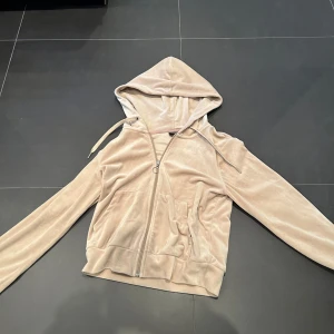 Beige hoodie med dragkedja - Säljer en mysig beige hoodie med dragkedja och huva. Den har långa ärmar och en praktisk ficka framtill. Perfekt för en avslappnad stil.