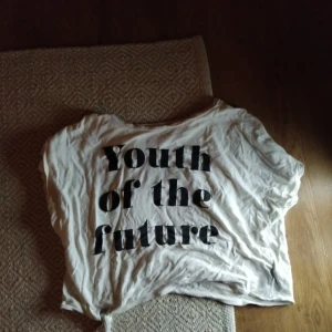 Croppad Vit t-shirt med text - Säljer en vit t-shirt med trycket 'Youth of the future' i svart. Perfekt för en avslappnad stil. T-shirten har korta ärmar, croppad och en rund halsringning. kontakta mig vid frågor om mer bilder, mått, pris osv🥰