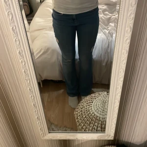 Blå jeans med slitningar - Snygga blå jeans med slitningar på låret. De har en bootcut-stil och är lågmidjade. Är i storlek L/34 men passar någon i storlek S eller M då de har krympt. Hålen har jag gjort själv, de finns vid knäet, och båda låren. 