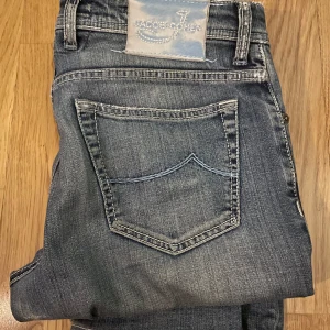 Jeans från Jacob Cohen - Snygga jeans från Jacob Cohen i en klassisk blå tvätt. De har en straight passform med knappgylf och femficksdesign.  De har lagats ett hål i skrevet men man märker inte av något 