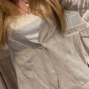 Beige kofta med knappar - Säljer en beige kofta med knappar framtill och praktiska fickor. Perfekt för en avslappnad stil. Koftan har trekvartsärmar