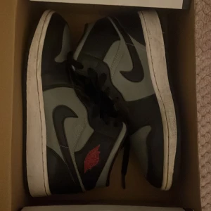 Nike Air Jordans i svart och grått - Säljer ett par Nike Air Jordans i svart och grått med klassisk design. Skorna har snörning och en röd detalj på sidan. Perfekta för sneakerheads som vill ha en stilren look.