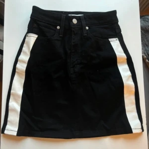 Svart jeanskjol från Calvin Klein - Svart jeanskjol från Calvin Klein med vita sidodetaljer. 