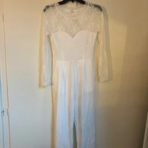 Vit spetsklänning med lång ärm - Elegant vit klänning med spetsdetaljer och lång ärm. Klänningen har en vacker öppen rygg och en figurnära passform. Perfekt för speciella tillfällen.
