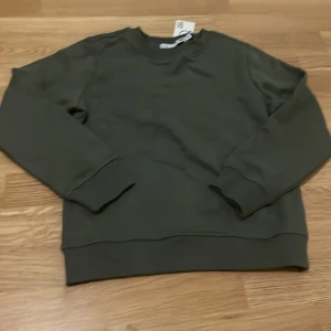 Grön sweatshirt från 157 - Säljer en stilren grön sweatshirt från 157. Tröjan har långa ärmar och en klassisk rund halsringning. Perfekt för en avslappnad look. Passar bra till både jeans och mjukisbyxor.