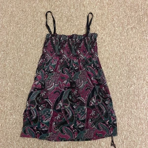 Mönstrad klänning/tröja från Lindex - Säljer en snygg mönstrad klänning från Lindex i storlek S. Klänningen har ett färgglatt paisleymönster i lila, grönt och svart. Den är axelbandslös med smala axelband och har en bekväm passform. Perfekt till sommaren att ha vanligt eller över en bikini!