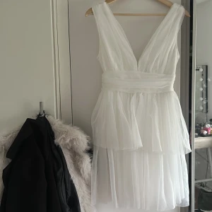 Studentklänning  - Elegant vit klänning med djup v-ringning och lager av tunt tyg som ger en luftig känsla. Den är ärmlös och har en markerad midja som framhäver figuren. Perfekt för sommarens speciella tillfällen. Säljer denna då jag valt att ha en lång klänning istället.💛💛