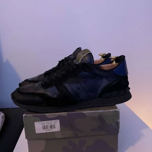 Valentino Garavani sneakers i svart och blått - Feta Valentino Garavani sneakers i svart och blått. Skorna är i bra skick och inga deffekter. Allt OG ingår 