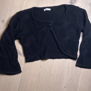 Svart stickad bolerotopp från Vila - Säljer en snygg svart stickad bolerotopp från Vila. Den har en knapp framtill och trekvartsärmar. Perfekt för att lägga till en extra touch till din outfit. Passar bra till både klänningar och toppar.