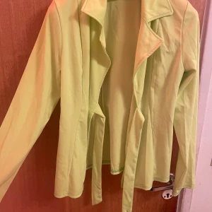 Limegrön tröja med knytband och byxan också  - Snygg limegrön set tröja med knytband i midjan med byxan. Perfekt för att lägga till en färgklick i garderoben. Tröjan har långa ärmar och en öppen design framtill.