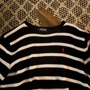Randig tröja från Polo Ralph Lauren - Snygg randig tröja från Polo Ralph Lauren i svart och vit med det klassiska röda logotypen på bröstet. Tröjan har långa ärmar och en ribbad halsringning. Perfekt för en stilren look.