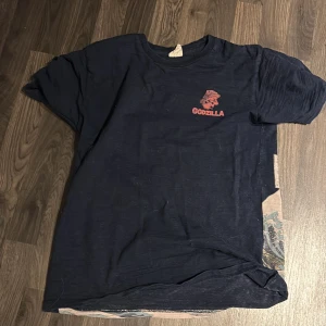 Mörkblå Godzilla t-shirt - Cool mörkblå t-shirt med Godzilla-tryck i rött på framsidan och ett stort motiv på baksidan. 