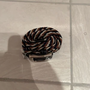 Flätat bälte med spänne - Säljer ett snyggt flätat bälte i flera färger som blå, brun och vit. Bältet har ett silverfärgat spänne och är perfekt för att ge en stilfull touch till din outfit. Det är flexibelt och justerbart för en bekväm passform.90 cm