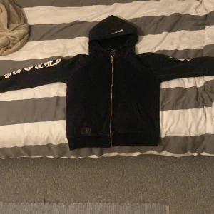 Svart hoodie från Chrome Hearts - Säljer en svart hoodie från Chrome Hearts med tryck på ryggen och ärmarna. Hoodien har en dragkedja framtill och text på huvan. Storlek m. Priset går att diskuteras 