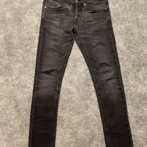 Svarta dondup jeans med slitningar - Snygga svarta jeans med en tight passform och coola slitningar på framsidank. Byxorna har  en diskret logga på bakfickan. Perfekta för en stilren look. Pris kan diskuteras!