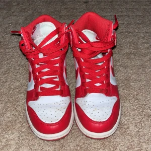 Rödvita Nike sneakers - Snygga rödvita Nike sneakers med hög design och klassisk snörning. Skorna har en vit bas med röda detaljer och Nike-logga. Perfekta för en sportig look. Jag köpte dom för 1500 så därför är dom lite dyrare. Tänker att man alltid kan buda ner.