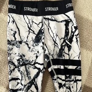 Mönstrade tights från Stronger - Snygga tights från Stronger med ett unikt marmorerat mönster i svart och vitt. De har en bred resår i midjan med logotypen 'STRONGER' tryckt runtom. Perfekta för träning eller en aktiv vardag.