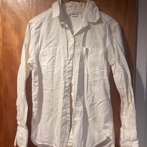 Vit linneskjorta från H&M - Säljer en stilren vit skjorta från L.O.G.G. i storlek XS/34. Skjortan är tillverkad av en linne- och bomullsblandning vilket ger en skön och luftig känsla. Den har långa ärmar och knappar framtill, perfekt för en avslappnad look.