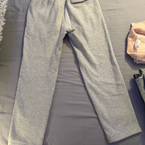 Grå mjukisbyxor från Nike - Säljer ett par grå mjukisbyxor från Nike med elastisk midja och en liten vit Nike-logga på benet. Perfekta för en avslappnad stil.