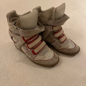 Beige Isabel Marant klackar med röda detaljer - Säljer ett par unika beige Isabel Marant skor med röda detaljer och kardborreband. Skorna har en hög design med vadderad plös och krage för extra komfort. Perfekta för en trendig look. Dom är äkta men köpta second hand. Om du vill ha fler bilder fixar jag de privat. Dustbags tillkommer vid köp
