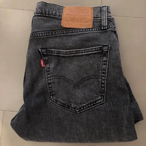 Svarta jeans från Levi's ett par 502 - Snygga svarta jeans från Levi's med klassisk femficksdesign och knappgylf. Perfekta för en stilren look. Levi's logga syns på bakfickan.