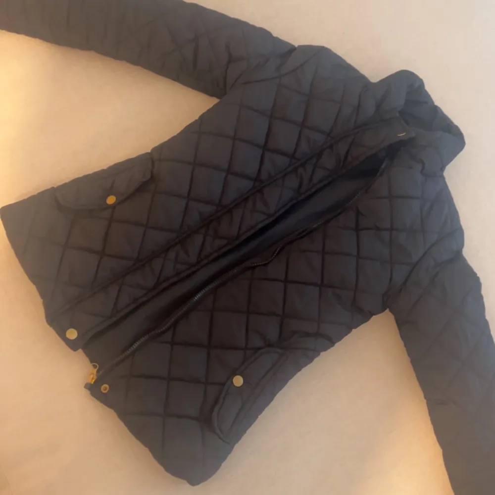 Snygg quiltad jacka med dragkedja och knappar. Jackan har en klassisk design med långa ärmar och en hög krage. Takit.