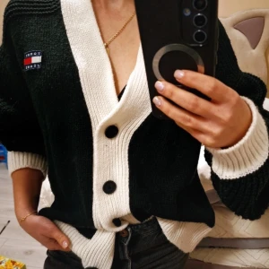 Svart och vit kofta från Tommy Jeans - Säljer en snygg svart och vit kofta från Tommy Jeans. Koftan har en ribbad struktur med stora knappar framtill och en broderad logga på bröstet. Oversized passform, storlek s på taggen men passar flexibelt S-L