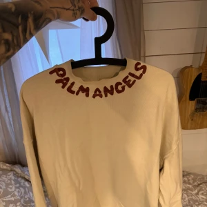 Beige tröja från Palm Angels - Säljer en stilren beige tröja från Palm Angels med deras logga i rött runt halsen. Kommer inte till användning då jag märkeskläder ej tilltalar mig på samma sätt som de gjorde förr. Hör av er vid intresse gött folk!